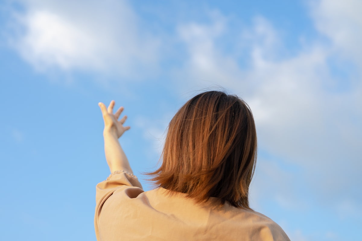 空に手を伸ばす女性の後ろ姿